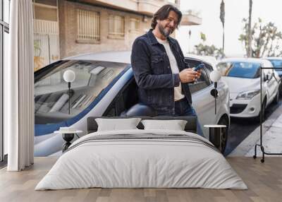 Middle age man using smartphone leaning on car at street Wall mural