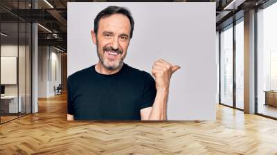 Middle age man wearing casual black t-shirt standing over isolated white background pointing thumb up to the side smiling happy with open mouth Wall mural