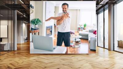 Middle age man with beard training and stretching doing exercise at home looking at sport video on computer Wall mural