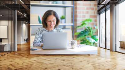 Middle age senior woman sitting at the table at home working using computer laptop with a happy face standing and smiling with a confident smile showing teeth Wall mural