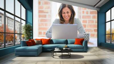 Middle age senior woman sitting at the table at home working using computer laptop with a happy face standing and smiling with a confident smile showing teeth Wall mural