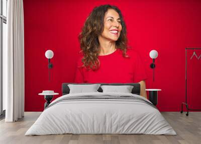 Middle age senior woman with curly hair over red isolated background looking away to side with smile on face, natural expression. Laughing confident. Wall mural