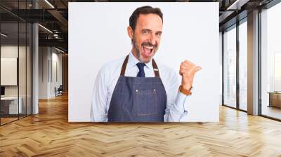 Middle age shopkeeper man wearing apron standing over isolated white background smiling with happy face looking and pointing to the side with thumb up. Wall mural