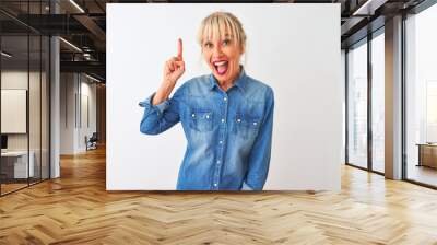 Middle age woman wearing casual denim shirt standing over isolated white background pointing finger up with successful idea. Exited and happy. Number one. Wall mural