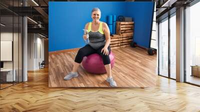 Middle age woman wearing sportswear sitting on fit ball at sport center Wall mural