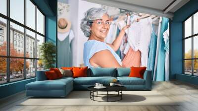 Middle age woman with grey hair at retail shop smiling happy looking at clothes Wall mural