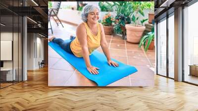 Middle age woman with grey hair smiling happy doing exercise and stretching on the terrace at home Wall mural