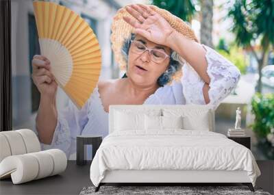 Middle age woman with grey hair using handfan on a very hot day of a heat wave Wall mural