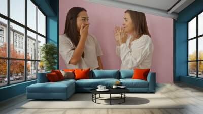 Mother and daughter sharing a moment of laughter against a pink wall, capturing family, love, and friendship between two women Wall mural