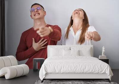 Mother and son standing together over isolated background laughing at you, pointing finger to the camera with hand over body, shame expression Wall mural