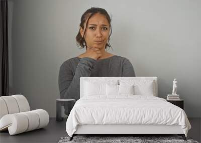 Pensive young hispanic woman in casual attire poses with crossed arms against a white backdrop, emanating a contemplative vibe. Wall mural