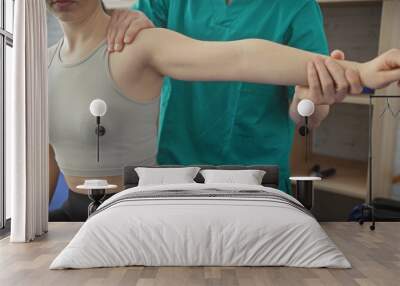 Physiotherapist in scrubs assists woman with arm exercise at rehabilitation center Wall mural