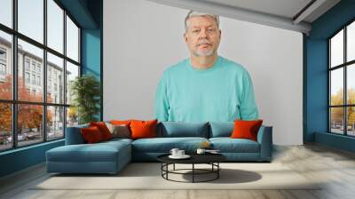 portrait of a grey-haired man in casual attire against a white background looking at the camera. Wall mural