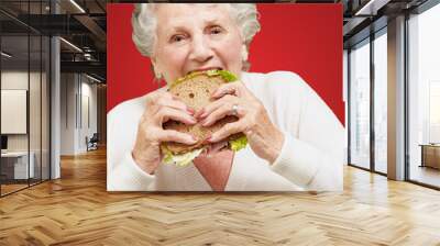 portrait of senior woman eating vegetal sandwich over red backgr Wall mural