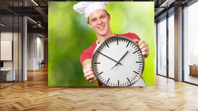 portrait of young cook man holding clock against a nature backgr Wall mural