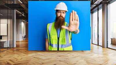 Redhead man with long beard wearing safety helmet and reflective jacket doing stop sing with palm of the hand. warning expression with negative and serious gesture on the face. Wall mural