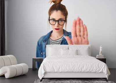 Redhead woman wearing striped t-shirt denim shirt and glasses over isolated white background doing stop sing with palm of the hand. Warning expression with negative and serious gesture on the face. Wall mural