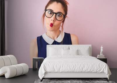 Redhead woman with pigtail wearing elegant dress and glasses over isolated pink background making fish face with lips, crazy and comical gesture. Funny expression. Wall mural