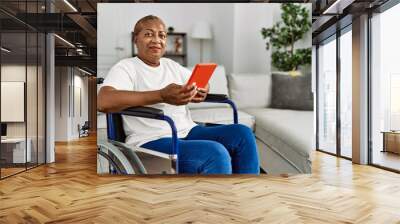 Senior african american woman using touchpad sitting on wheelchair at home Wall mural