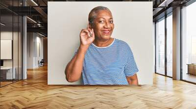 Senior african american woman wearing casual clothes smiling with hand over ear listening and hearing to rumor or gossip. deafness concept. Wall mural