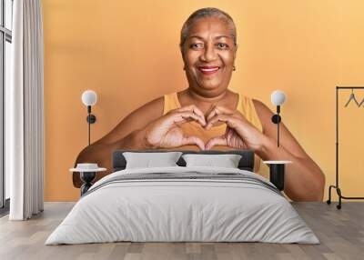 Senior african american woman wearing casual style with sleeveless shirt smiling in love doing heart symbol shape with hands. romantic concept. Wall mural