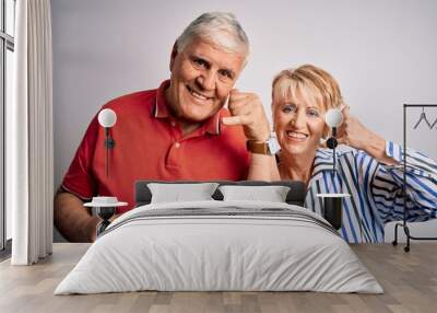 Senior beautiful couple standing together over isolated white background smiling doing phone gesture with hand and fingers like talking on the telephone. Communicating concepts. Wall mural