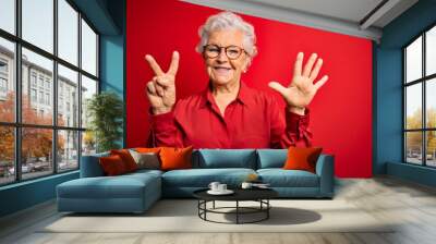 Senior beautiful grey-haired woman wearing casual shirt and glasses over red background showing and pointing up with fingers number seven while smiling confident and happy. Wall mural