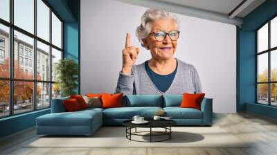 Senior beautiful grey-haired woman wearing casual sweater and glasses over white background pointing finger up with successful idea. Exited and happy. Number one. Wall mural