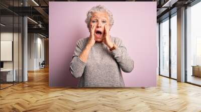 Senior beautiful woman wearing casual t-shirt standing over isolated pink background afraid and shocked, surprise and amazed expression with hands on face Wall mural