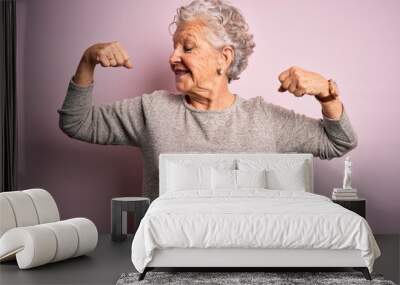 Senior beautiful woman wearing casual t-shirt standing over isolated pink background showing arms muscles smiling proud. Fitness concept. Wall mural