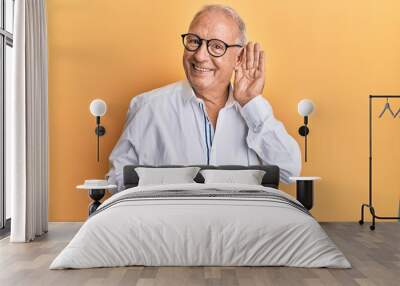 Senior caucasian man wearing casual clothes and glasses smiling with hand over ear listening and hearing to rumor or gossip. deafness concept. Wall mural