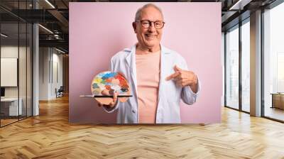 Senior grey haired artist man painting using painter palette over pink background with surprise face pointing finger to himself Wall mural