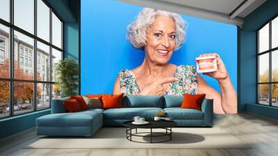 Senior grey-haired woman holding denture smiling happy pointing with hand and finger Wall mural