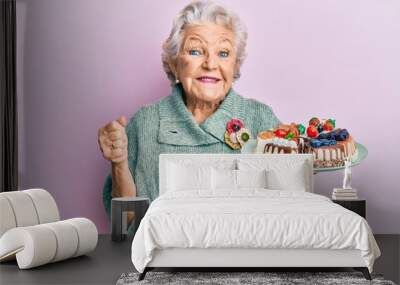 Senior grey-haired woman holding plate with cake slices screaming proud, celebrating victory and success very excited with raised arm Wall mural