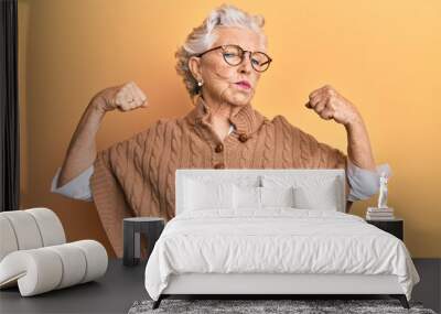 Senior grey-haired woman wearing casual clothes and glasses showing arms muscles smiling proud. fitness concept. Wall mural