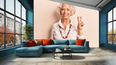 Senior grey-haired woman wearing casual clothes smiling with happy face winking at the camera doing victory sign. number two. Wall mural