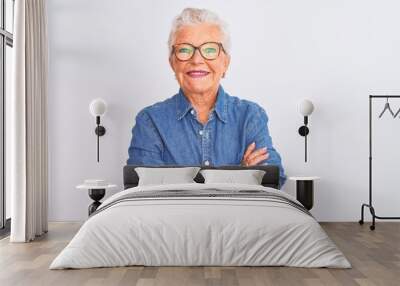 Senior grey-haired woman wearing denim shirt and glasses over isolated white background happy face smiling with crossed arms looking at the camera. Positive person. Wall mural