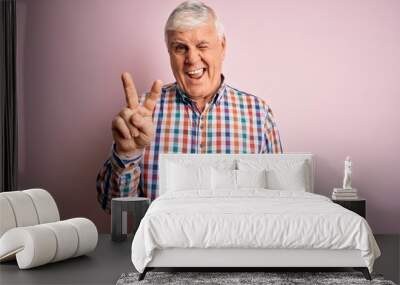 Senior handsome hoary man wearing casual colorful shirt over isolated pink background smiling with happy face winking at the camera doing victory sign with fingers. Number two. Wall mural