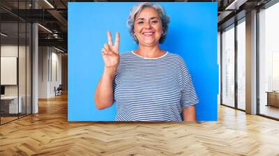 Senior hispanic grey- haired woman wearing casual clothes smiling with happy face winking at the camera doing victory sign. number two. Wall mural