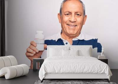 Senior man with grey hair holding bottle of pills smiling happy pointing with hand and finger Wall mural