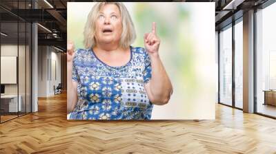 Senior plus size caucasian woman over isolated background amazed and surprised looking up and pointing with fingers and raised arms. Wall mural