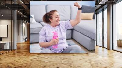 Senior woman sitting on floor doing strong gesture with arm at home Wall mural