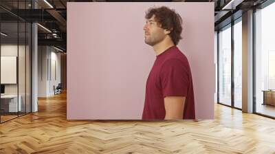 Side-profile of a young bearded man in casual attire isolated against a pink wall background, portrays a relaxed adult male. Wall mural