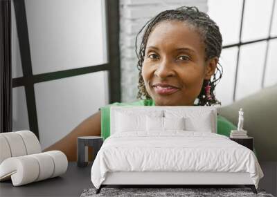 Smiling african american woman in green top enjoying a relaxed day in a bright living room setting. Wall mural