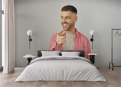 Smiling hispanic man with beard in casual attire pointing playfully against a white background Wall mural