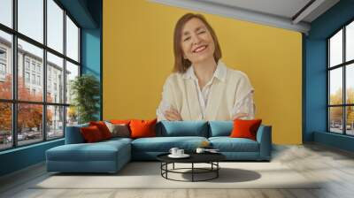 Smiling middle-aged woman with short hair, dressed in white, standing confidently against a yellow background. Wall mural