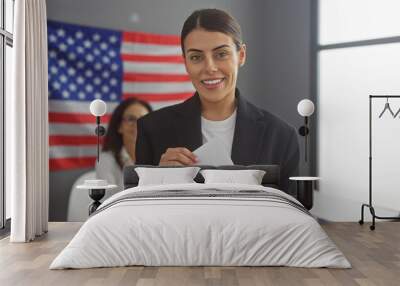 Smiling woman holding envelope with another woman and american flag in background at electoral center. Wall mural