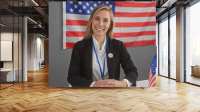 Smiling woman with a 'voted' sticker, american flag backdrop in a voting center. Wall mural