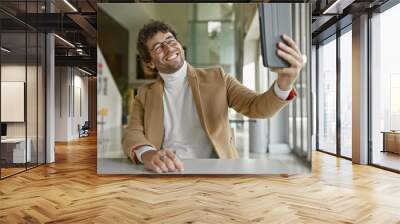 Smiling young hispanic man with beard takes a selfie in a modern office interior. Wall mural