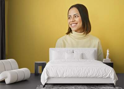 Smiling young hispanic woman in beige sweater against a vibrant yellow background looking to the side. Wall mural